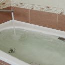 A bathtub with the faucet still running. The water level is just about full, meaning that overflowing is about to begin.