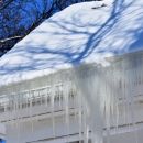 A closeup of a snowy roof and gutter system with a large ice damn hanging off the side of the roof.