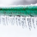 A close up of a frozen green pipe with icicles hanging off of it.