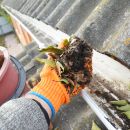 A closeup view of a person wearing orange gloves pulling a pile of debris out of their gutter system