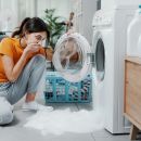 A woman in an orange shirt looks in awe as her washing machine overflows