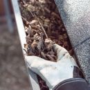 A top view of a man with white gloves cleaning leaves and debris out of the rain gutters