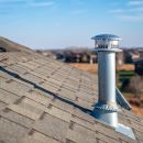 A close up image of a chimney exhaust on an asphalt roof.