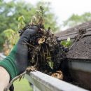 A person using their garden gloves to remove dirt and debris from gutters, a crucial step in spring preparation